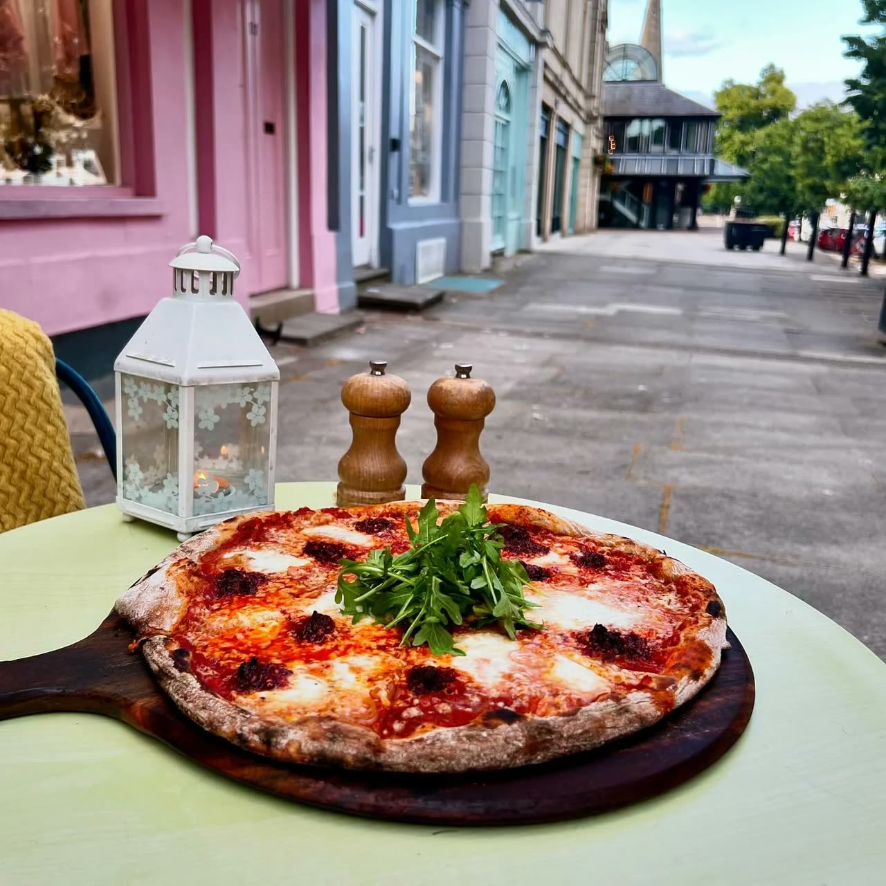 A sourdough nduja pizza on a board at a table outside